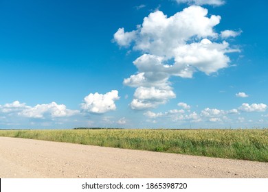 Empty dirt road through the fields. Fluffy clouds on a warm summer Sunny day over a field of wheat. Pure nature away from the big city. Eco tourism.