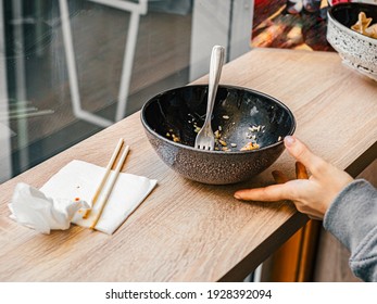 Empty dirty black plate after meal with fork inside next to napkins with chopsticks, girl's hand. After meal concept. Background from wooden table by window in cafe - Powered by Shutterstock