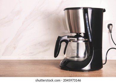 Empty drip coffee maker on kitchen wooden countertop against marble backdrop. 