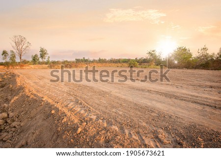 Empty dry cracked swamp reclamation soil, land plot for housing construction project with car tire print in rural area and beautiful sun set with fresh air Land for sales landscape concept