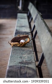 Empty dug out bench at a baseball field with a lone baseball glove and baseball sitting in the middle.