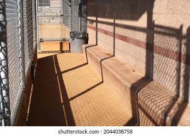 An empty dugout at a ball field. Chain link fence and shadows. Lighting at dusk.                             - Powered by Shutterstock