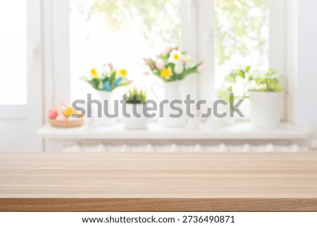 Empty easter table background in front of deeply blurred colorful flowers and painted eggs on kitchen window sill