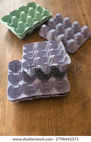 Empty egg cartons made of molded paper pulp, in pastel colors, on a wooden table