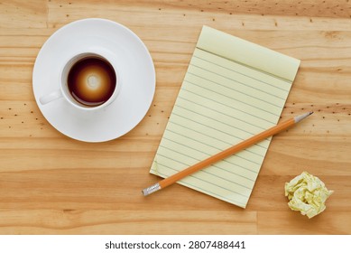 Empty espresso coffee cup, notepad and pencil on pine wood table