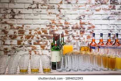 Empty and filled glasses next to bottles of alcoholic beverages on a brick wall background. Banquet or party preparations.