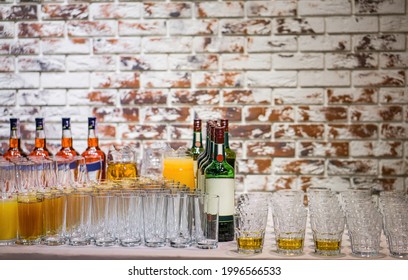 Empty and filled glasses next to bottles of alcoholic beverages on a brick wall background. Banquet or party preparations.