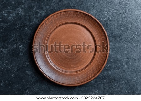 Empty flat plate of red clay over black background . Top view, close up . Rough ceramic bowl background with copy space