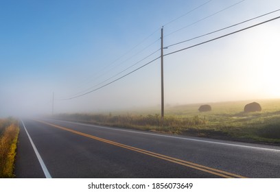 Empty, Foggy, Rural Farm Country Road In The Early Morning Sunlight With Powerlines