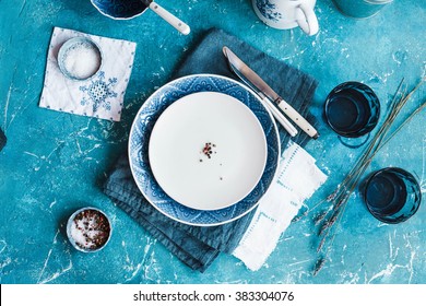 Empty Food Tableware, Ceramic Plate, Spice Little Bowls, Knife, Fork With A Old Linen Cloth On A Old Vintage Stone Table. Country Blue Styling. Top View.