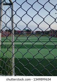 Empty Football Field With Synthetic Grass, Seen From Behind The Iron Fence Beside The Goalpost