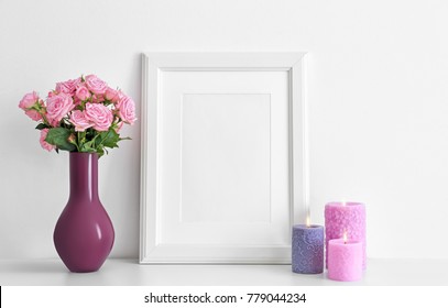 Empty frame, pink roses and candles on table near white wall - Powered by Shutterstock