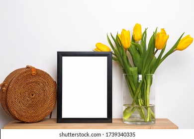 Empty frame standing on small wooden table with yellow tulips and straw bag. Summer composition - Powered by Shutterstock