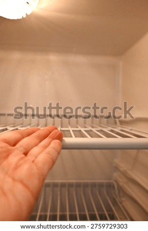 Empty fridge with hand pointing inside representing food shortage and cost of living crisis. Concept of financial hardship, poverty and limited resources in household.