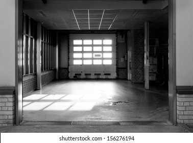 Empty Garage At Ambulance Station With Bright Sunlight Coming Though Panels In Overhead Door And Small Patch Of Leaked Oil On Floor.