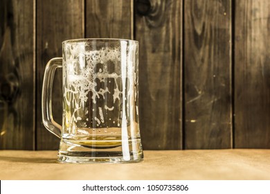 Empty glass of beer on a table, against a wooden plank of a pub.