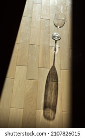 An Empty Glass Casting A Shadow On The Stave Oak Floor. 