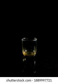 An Empty Glass With Yellow On Bottom In The Dark