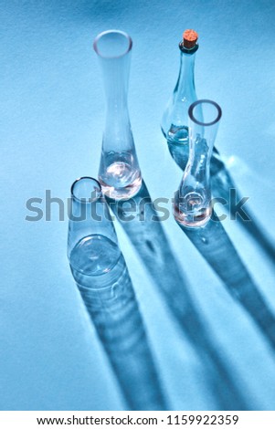 Empty glasses with diagonal long shadows on light blue paper background, space for text. Test glass flask in research laboratory.
