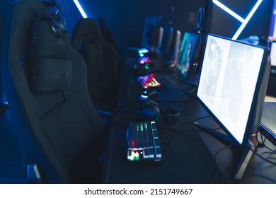 Empty Glow Neon Illuminated Cybercafe Room With Computers On Tables, Professional Seats, And Illuminated Keyboards No People. Modern Cyber Sport. High Quality Photo