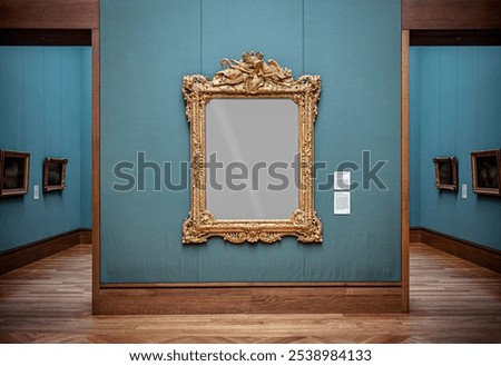 Empty gold ornate mirror hanging on a teal wall in a museum gallery with other artwork visible in adjacent rooms and wooden parquet floors