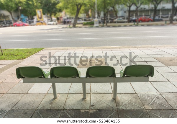 empty\
green chair at the public bus stop on the\
footpath.