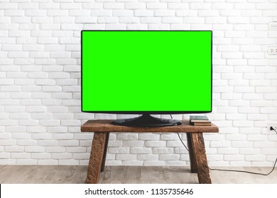 Empty Green Flat TV Screen On Wood Stand Over A White Brick Wall.