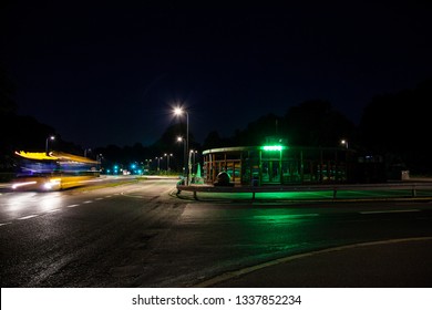 An Empty Green Light Cafe And Next To It A Vividly Colorful Bus Passing On An Empty Suburban Street At Night As A Ray Of Light Due To Long Exposure