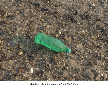 Empty green plastic bottle on the beach, concept of keeping the environment clean, no trash on the beach