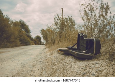 Empty Guitar Case Next To A Dusty Road. This Vintage Retro Shot Is Perfect For Countrymusic, Natural, Dusty Music Background. Vintage Farmland Picture.