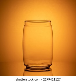 Empty Heat-resistant Glass Jar Standing On A Black Mirrored Table Backlit With Orange Light