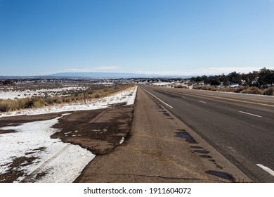 Empty Highway Cutting Through Snow Covered Wide Open Desert Vista On Clear Day In Rural New Mexico