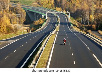 Empty Highway Leading Across The Bridge Over The Valley, In The Foreground Riding A Motorcycle, Electronic Toll Gates, Deciduous Forest In Autumn Colors, View From Above