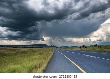 Empty highway stretching through open countryside under dramatic storm clouds. Dark, heavy skies contrast with the quiet rural road, creating a powerful mood of tension, anticipation, and solitude. Ideal for concepts related to travel, journey, uncertainty, weather, climate, and freedom.