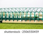 Empty horse racing starting stalls waiting for riders.
Green colored starting gate on start by tractor machine at equiestrian racehorse hippodrome. Outdoor sport racecourse competition equipment