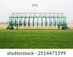 Empty horse racing starting stalls waiting for riders.
Green colored starting gate on start by tractor machine at equiestrian racehorse hippodrome. Outdoor sport racecourse competition equipment