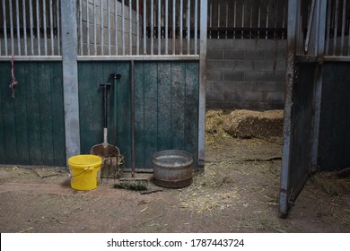 Empty horse stable stall. To be prepared for horses with straw to put as bedding. Fork, brush, shovel, feed bowl and water bucket at the stable entrance. 