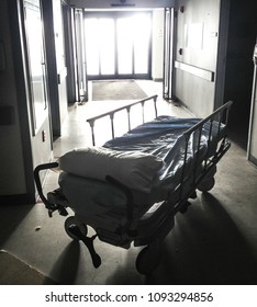 An Empty Hospital Gurney Sits Alone In A Brightly Lit Corridor.