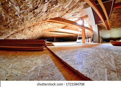 Empty house attic space with wood beams, wool roof insulation, chipboard floor and roof window with sunlight.