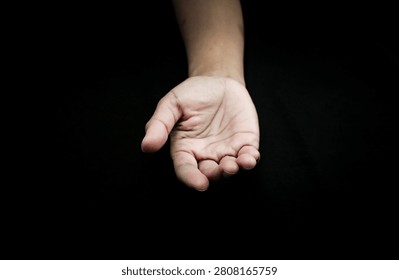 An empty human hand reaching forward with an open, slightly cupped palm, reaching out or presenting nothing against a solid black background.