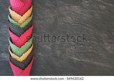 Empty ice cream cones in assorted colors on rustic surface. Top view, dark toned image, blank space