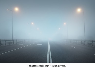 An empty illuminated asphalt road (highway) in a thick fog. Pedestrian walkway, crossing, street lights. Dangerous driving, walking, cycling, traffic laws concepts - Powered by Shutterstock
