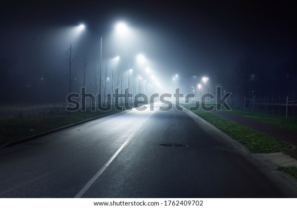 An empty illuminated\
motorway in a fog at night. Road sign close-up. Dark urban scene,\
cityscape. Riga, Latvia. Dangerous driving, speed, freedom, concept\
image