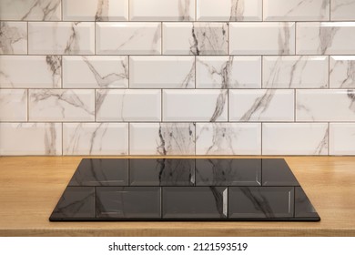 Empty induction cooker hob closeup in wooden counter and white tile backsplash