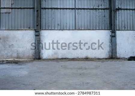 Empty industrial warehouse interior featuring a worn concrete floor, corrugated metal walls, and grunge textures. Spacious factory or storage background with copy space, suitable for industrial, logistics, manufacturing, construction, or urban-themed projects.