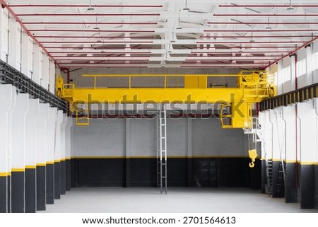 Empty industrial workshop with an overhead crane fire safety system red pipes. A bright yellow crane is suspended from the ceiling. Concept of industry, manufacturing, engineering, interior