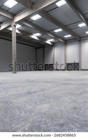 The empty interior of a large industrial warehouse. The concrete industrial hall is flooded with natural light.