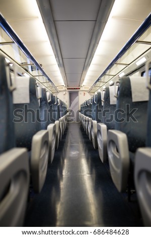 Empty interior of a passenger train car aka coach or carriage . Rows of unoccupied seats and folding tables in economy or second class.
