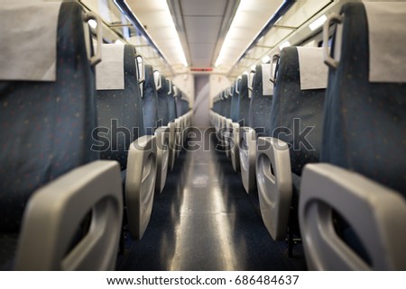 Empty interior of a passenger train car aka coach or carriage . Rows of unoccupied seats and folding tables in economy or second class.