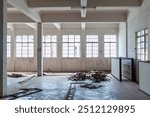 An empty interior space with large windows, debris, and exposed architecture creating a raw industrial aesthetic.